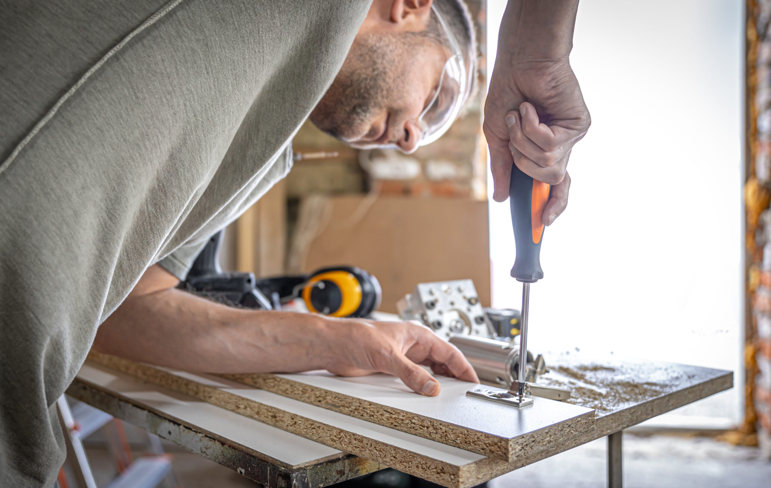 Screwing a self-tapping screw into a metal fastening hole on a wood strip using a screwdriver, the work of a carpenter.