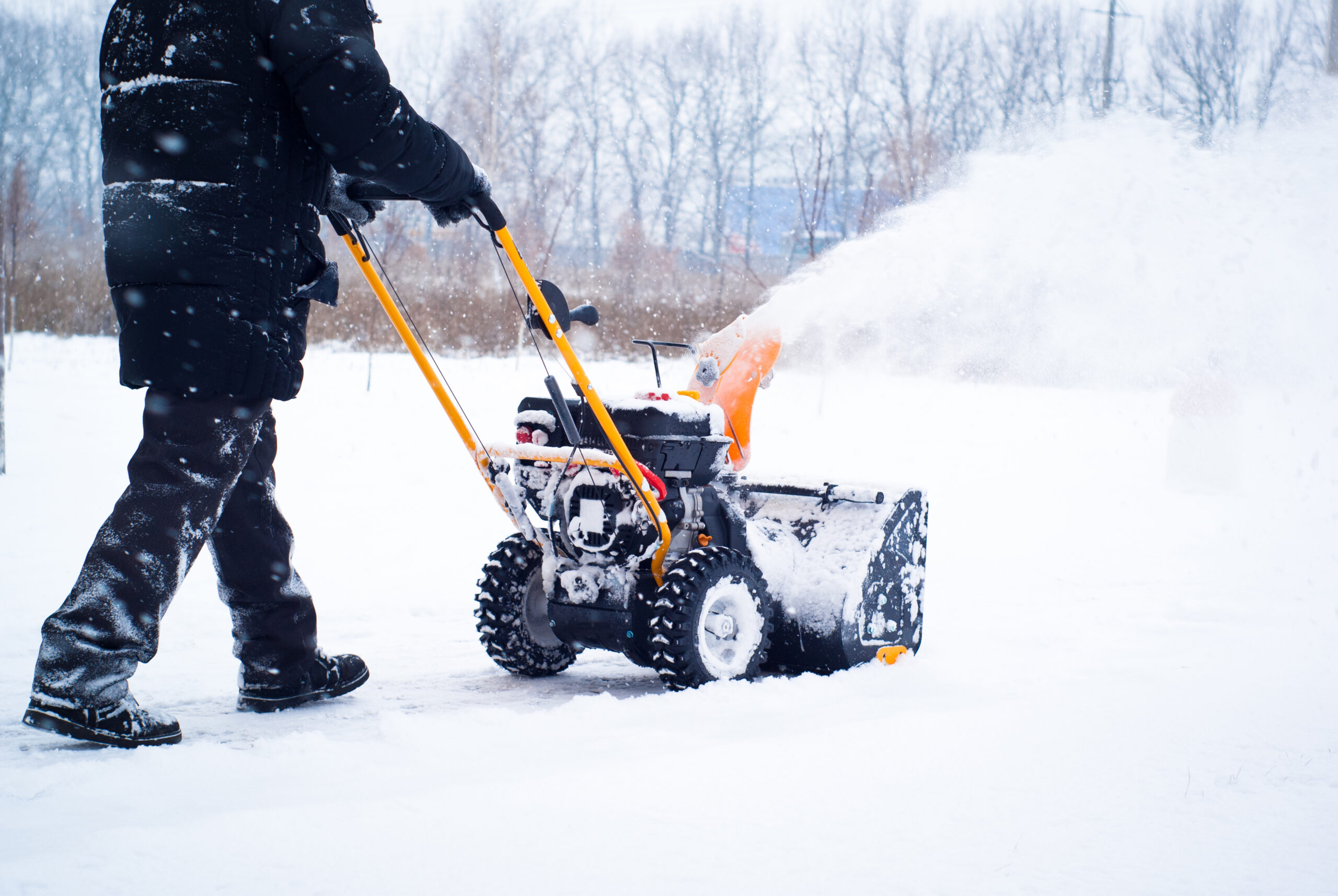 A man cleans snow from sidewalks with snowblower.